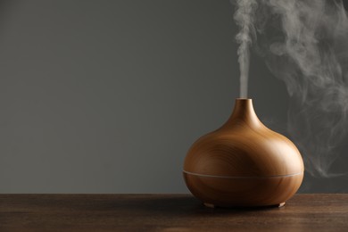 Photo of Aroma oil diffuser with steam on wooden table, space for text