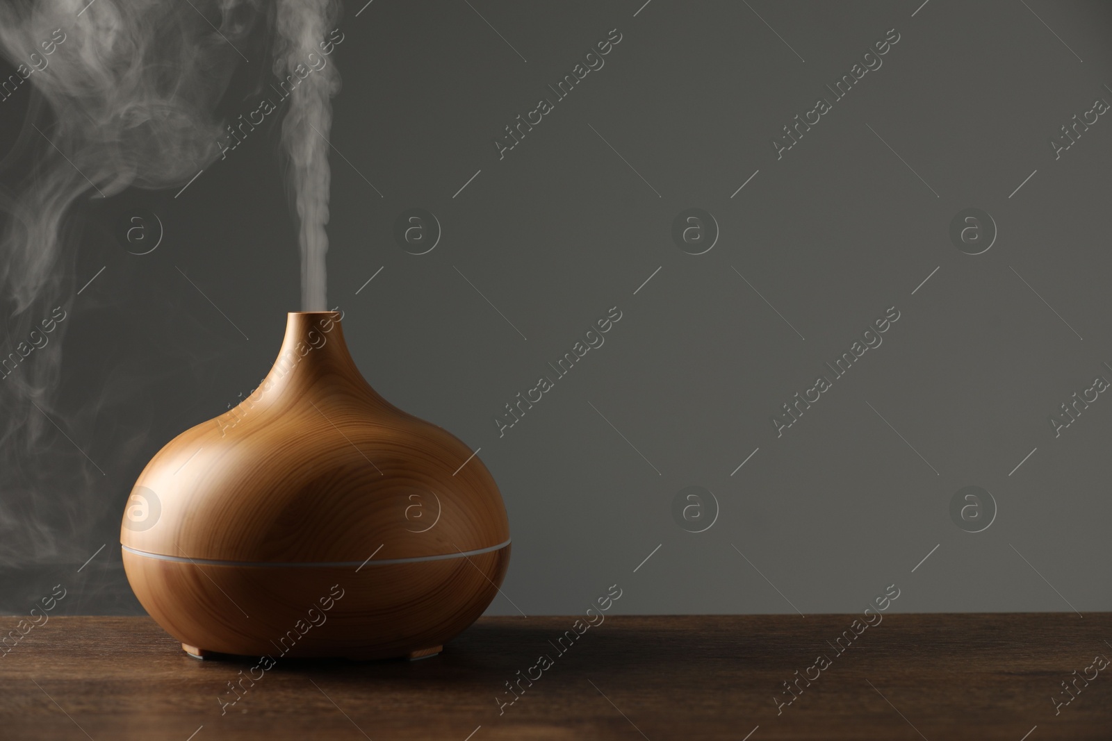 Photo of Aroma oil diffuser with steam on wooden table, space for text