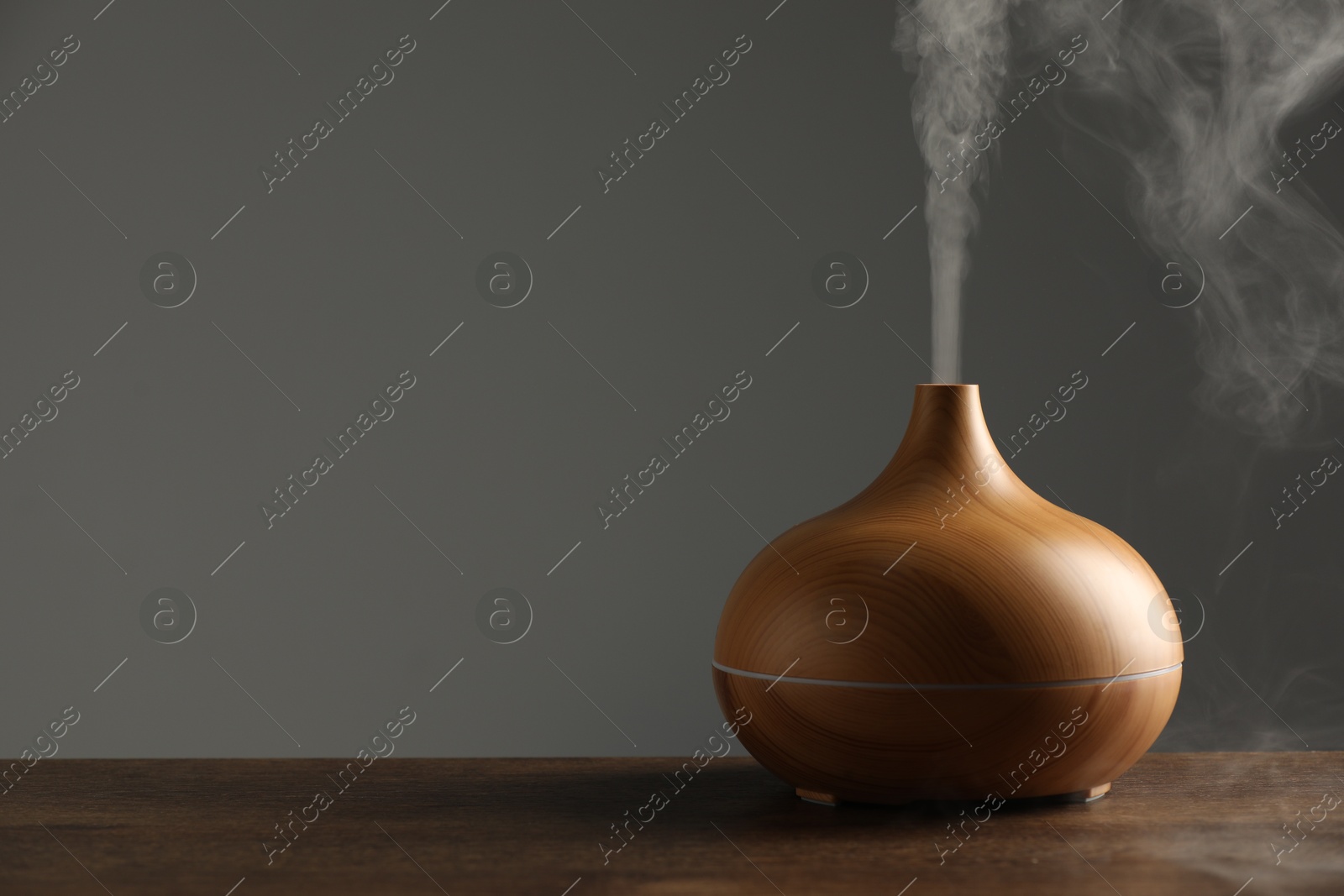 Photo of Aroma oil diffuser with steam on wooden table, space for text