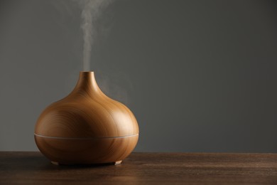 Photo of Aroma oil diffuser with steam on wooden table, space for text