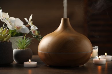 Aroma oil diffuser, burning candles and houseplants on wooden table, closeup