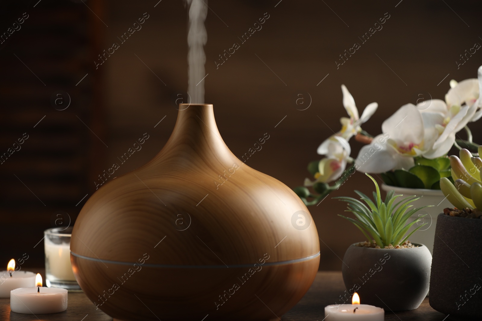 Photo of Aroma oil diffuser, burning candles and houseplants on wooden table