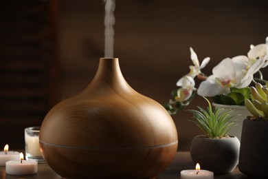 Photo of Aroma oil diffuser, burning candles and houseplants on wooden table