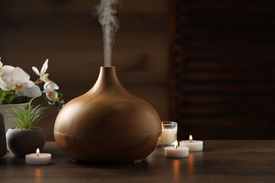 Photo of Aroma oil diffuser, burning candles and houseplants on wooden table