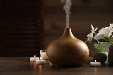 Photo of Aroma oil diffuser, burning candles and houseplants on wooden table