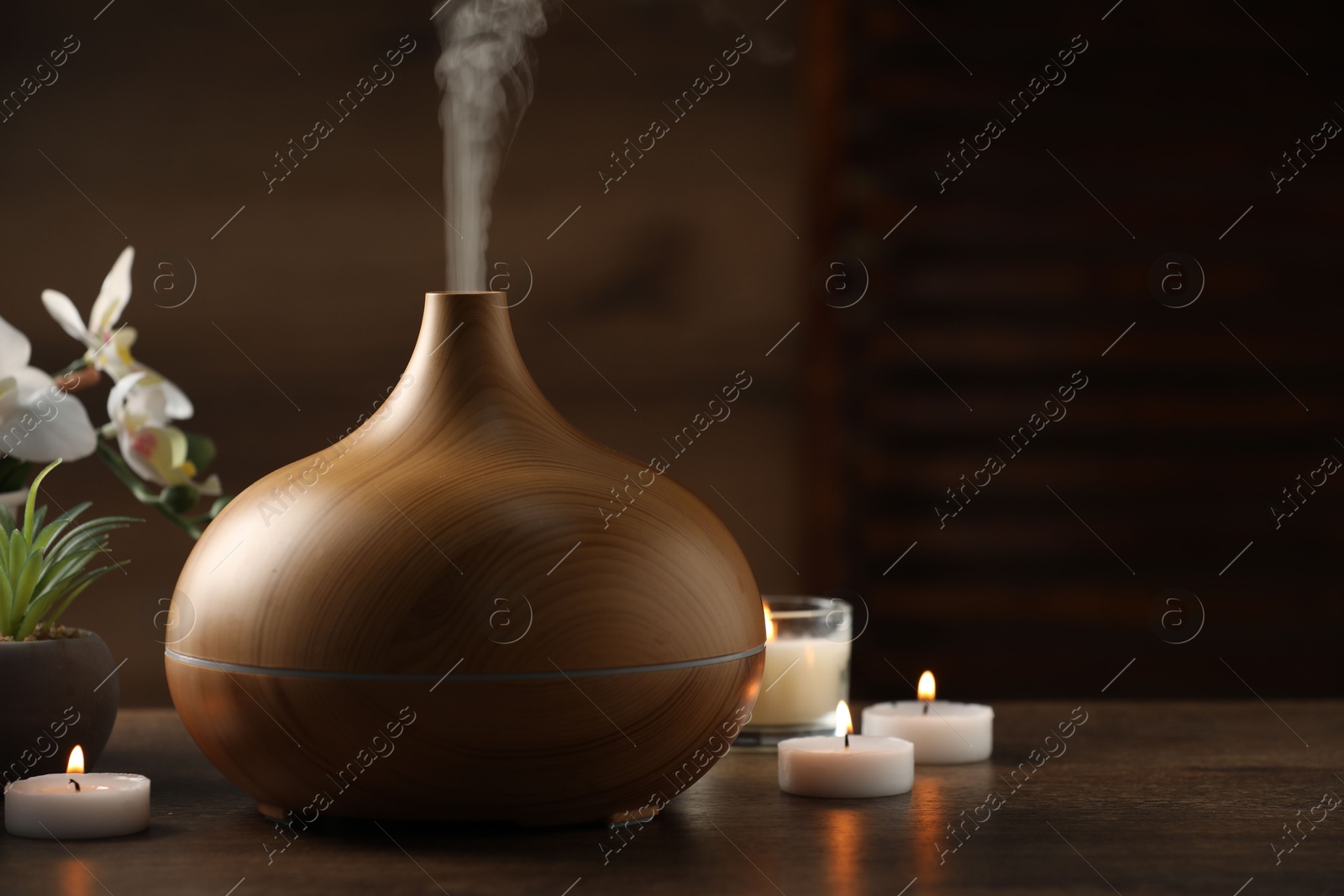 Photo of Aroma oil diffuser, burning candles and houseplants on wooden table, space for text