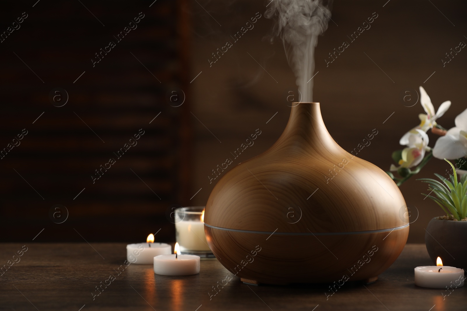 Photo of Aroma oil diffuser, burning candles and houseplants on wooden table, space for text