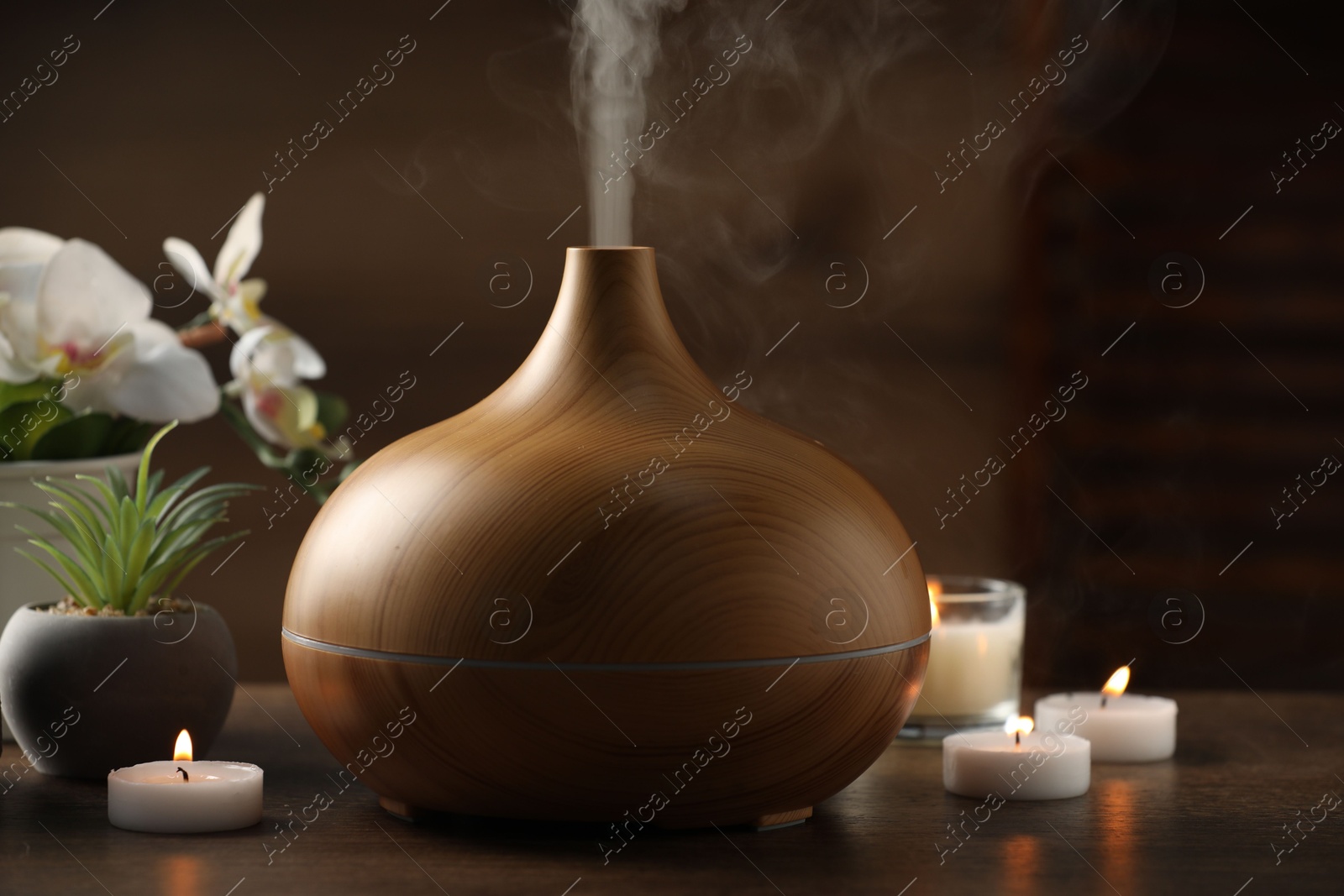 Photo of Aroma oil diffuser, burning candles and houseplants on wooden table, closeup