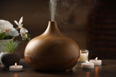 Aroma oil diffuser, burning candles and houseplants on wooden table, closeup