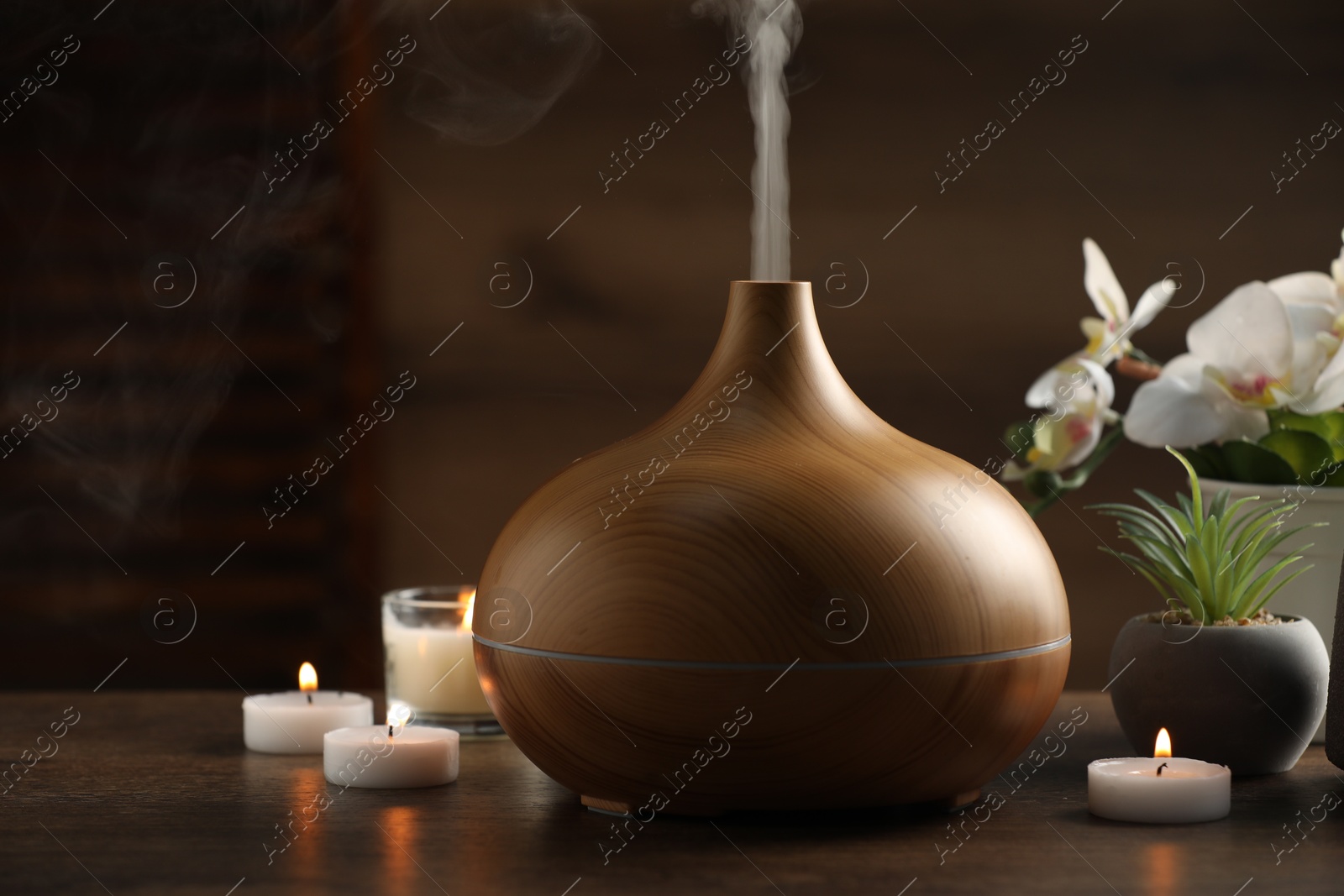 Photo of Aroma oil diffuser, burning candles and houseplants on wooden table