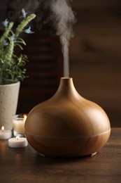 Photo of Aroma oil diffuser, burning candles and houseplants on wooden table