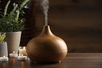 Aroma oil diffuser, burning candles and houseplants on wooden table, space for text