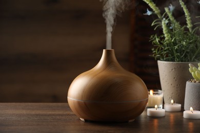 Aroma oil diffuser, burning candles and houseplants on wooden table, space for text