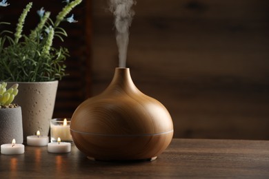 Aroma oil diffuser, burning candles and houseplants on wooden table, space for text