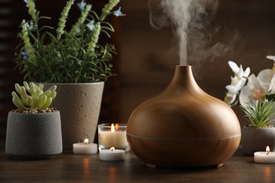 Photo of Aroma oil diffuser, burning candles and houseplants on wooden table