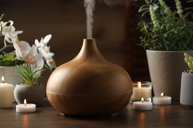 Photo of Aroma oil diffuser, burning candles and houseplants on wooden table