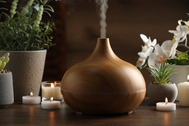 Photo of Aroma oil diffuser, burning candles and houseplants on wooden table