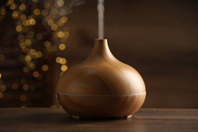 Photo of Aroma oil diffuser on wooden table against blurred lights