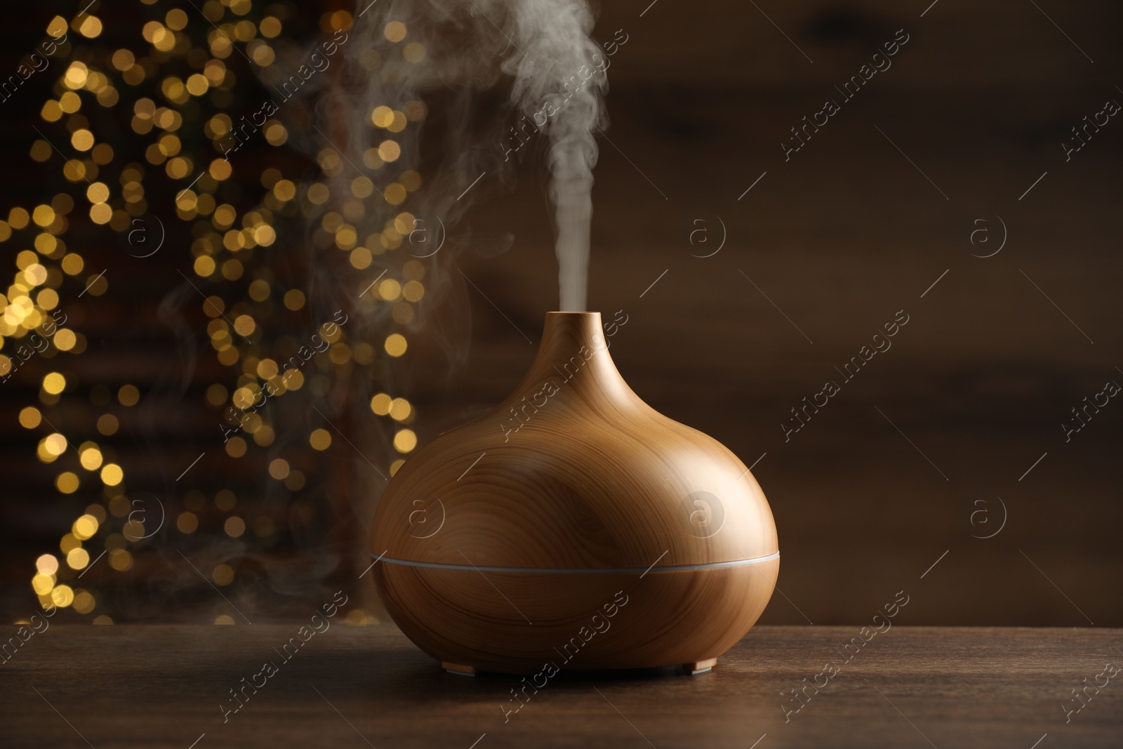 Photo of Aroma oil diffuser on wooden table against blurred lights