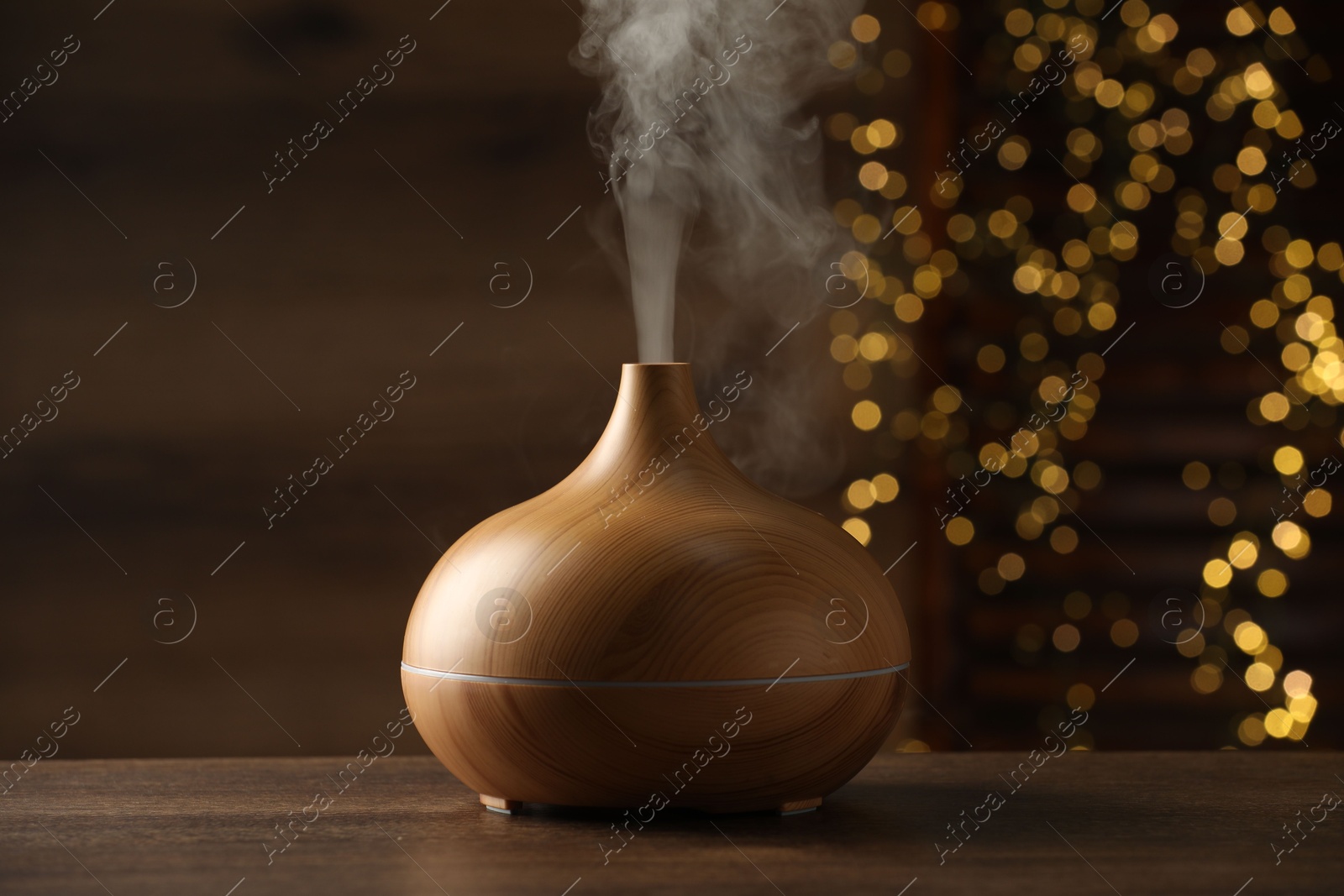 Photo of Aroma oil diffuser on wooden table against blurred lights