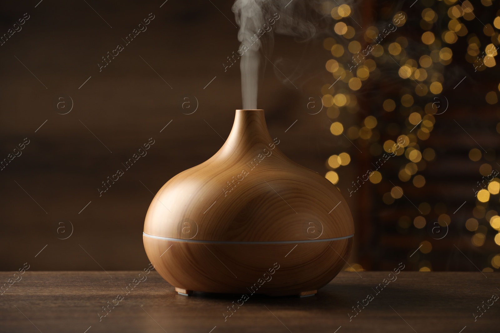 Photo of Aroma oil diffuser on wooden table against blurred lights