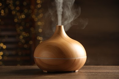 Aroma oil diffuser on wooden table against blurred lights