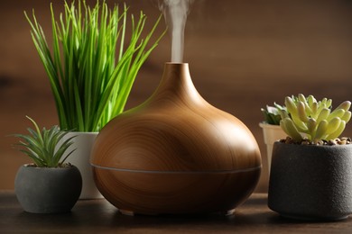 Aroma oil diffuser and houseplants on wooden table