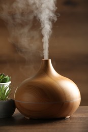 Aroma oil diffuser and houseplants on wooden table