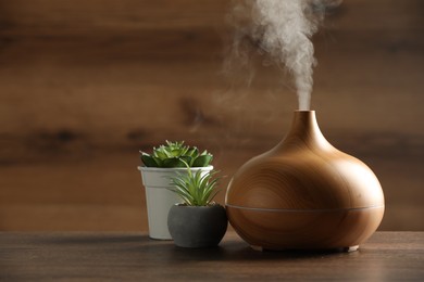 Photo of Aroma oil diffuser and houseplants on wooden table, space for text