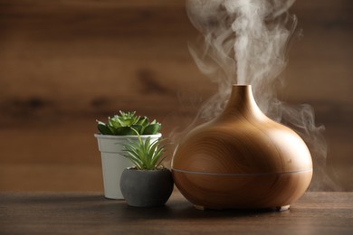 Aroma oil diffuser and houseplants on wooden table