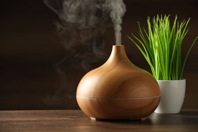 Aroma oil diffuser and plant on wooden table, space for text