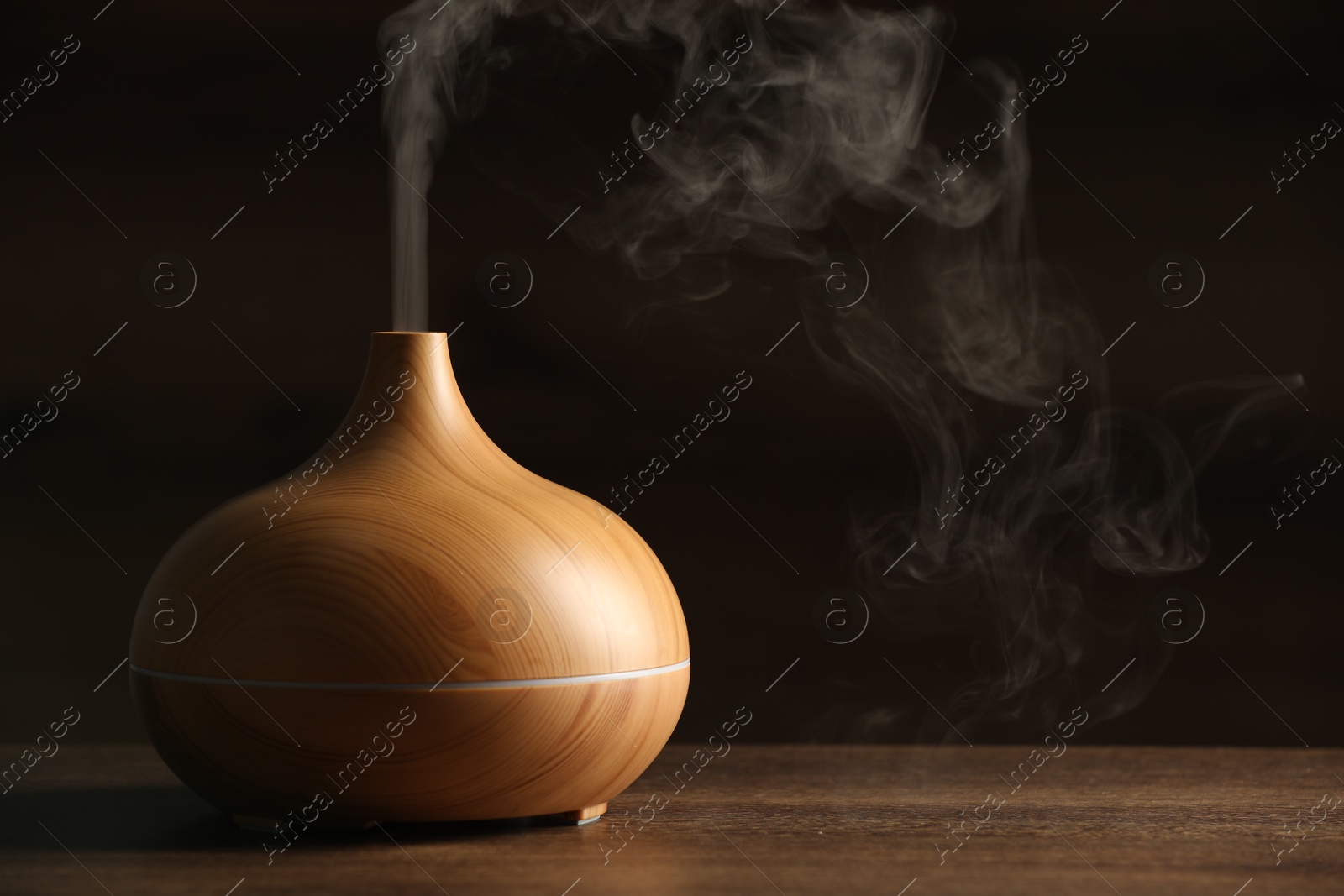 Photo of Aroma oil diffuser with steam on wooden table, space for text