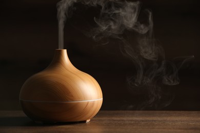 Photo of Aroma oil diffuser with steam on wooden table, space for text