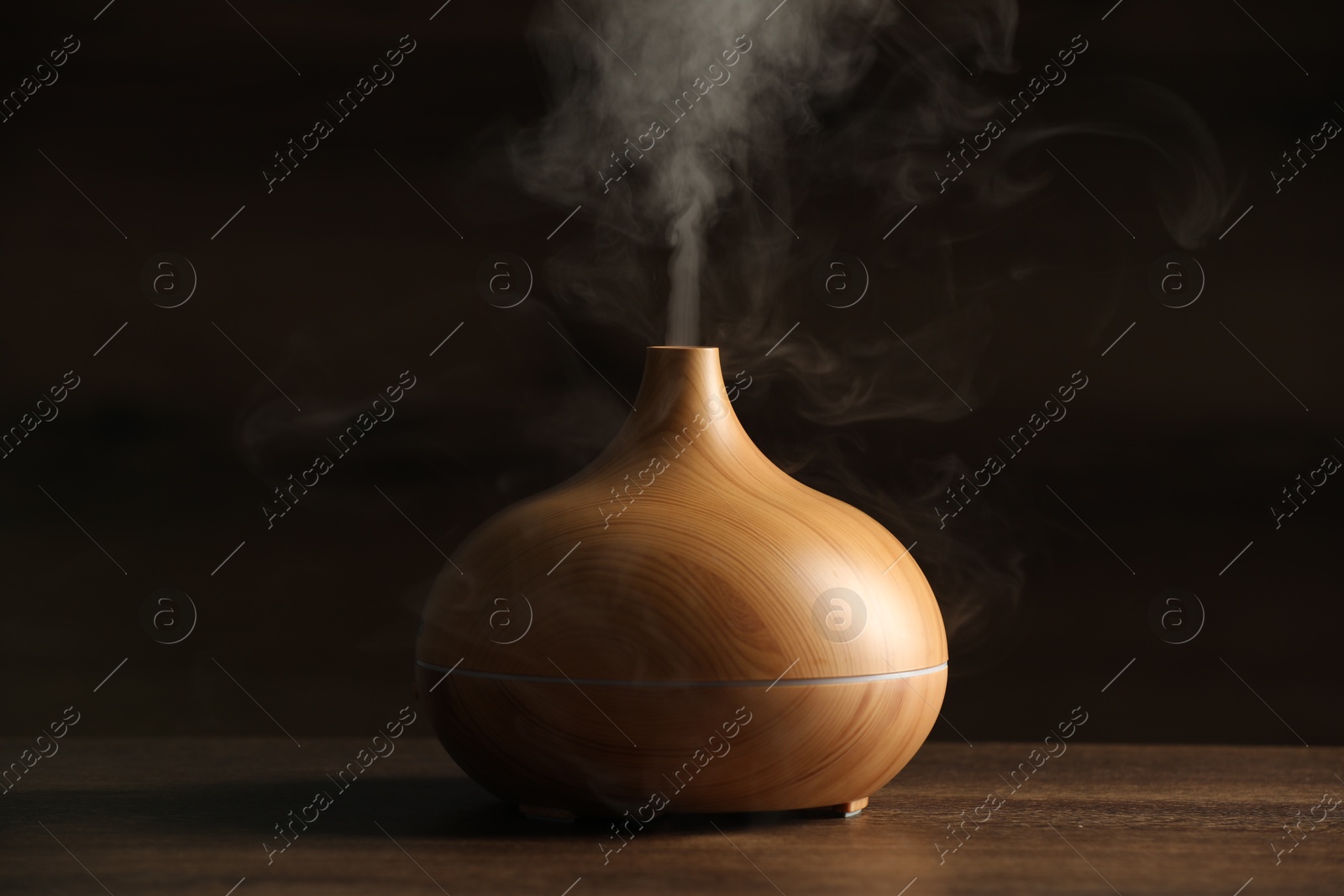 Photo of Aroma oil diffuser with steam on wooden table