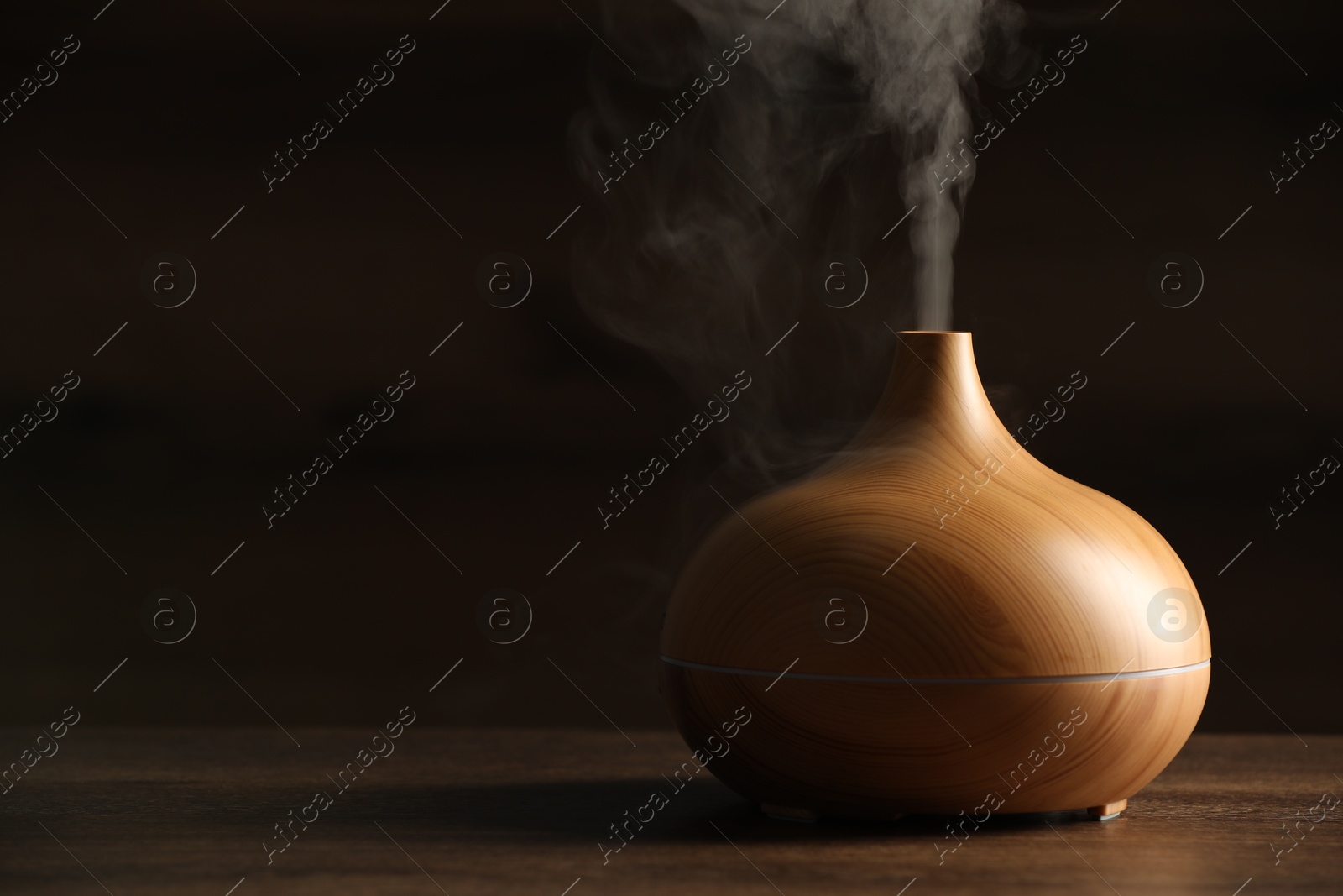 Photo of Aroma oil diffuser with steam on wooden table, space for text