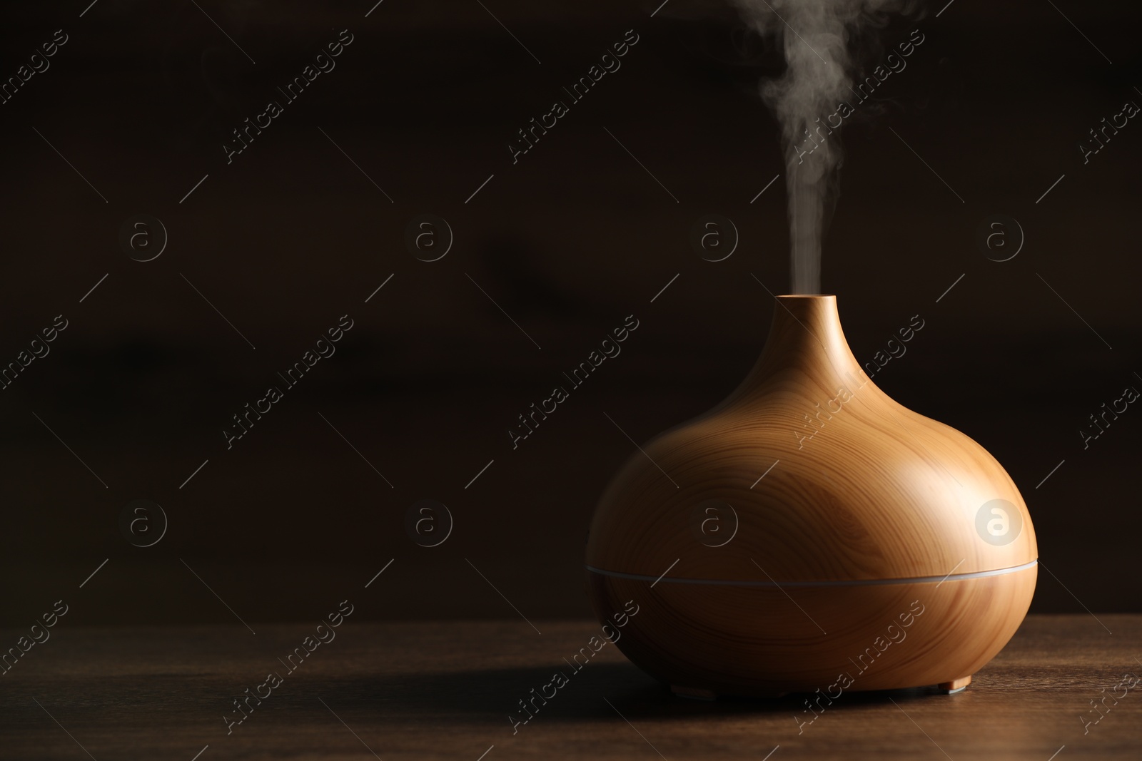 Photo of Aroma oil diffuser with steam on wooden table, space for text