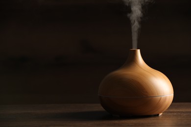 Aroma oil diffuser with steam on wooden table, space for text