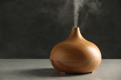 Aroma oil diffuser with steam on light grey table, space for text