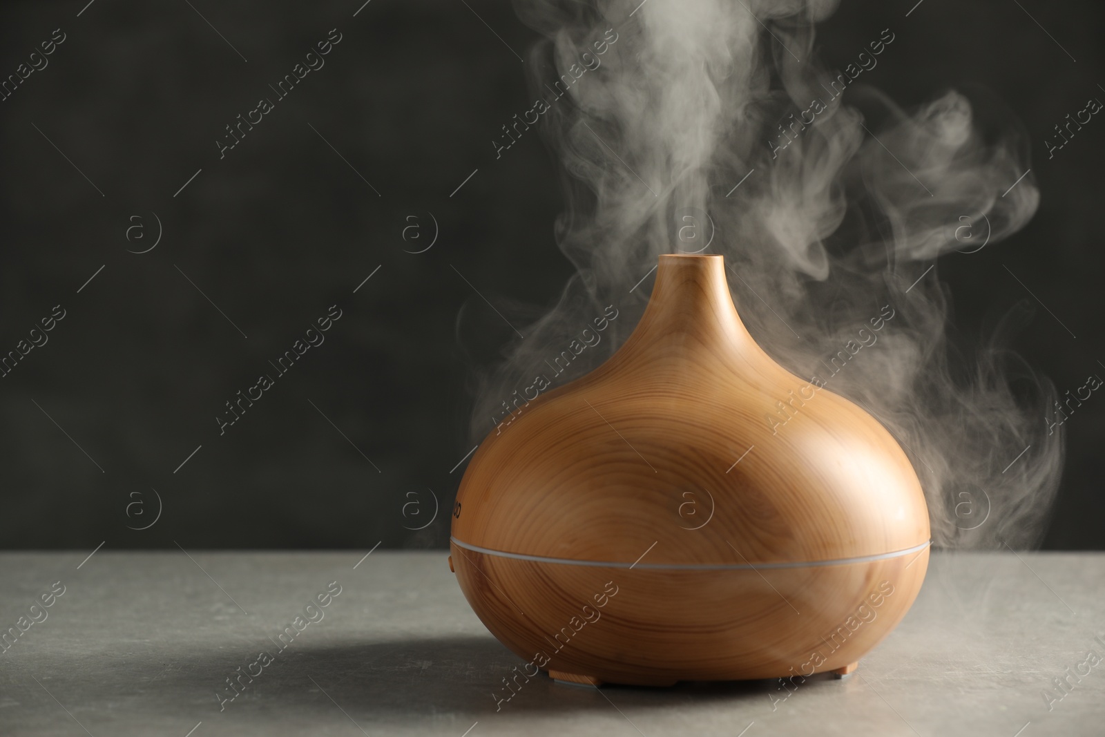 Photo of Aroma oil diffuser with steam on light grey table, space for text