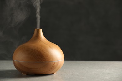 Photo of Aroma oil diffuser with steam on light grey table, space for text