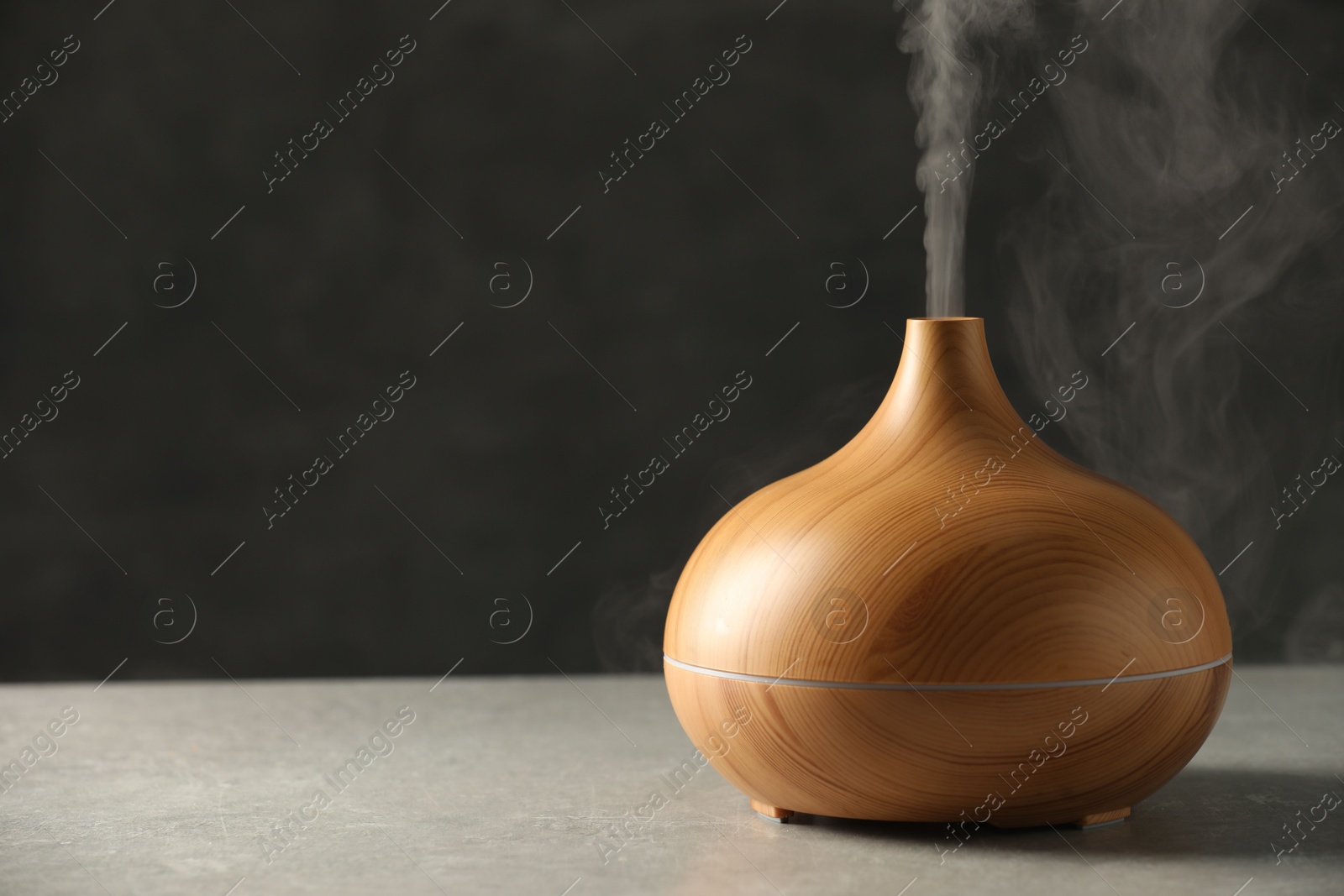 Photo of Aroma oil diffuser with steam on light grey table, space for text