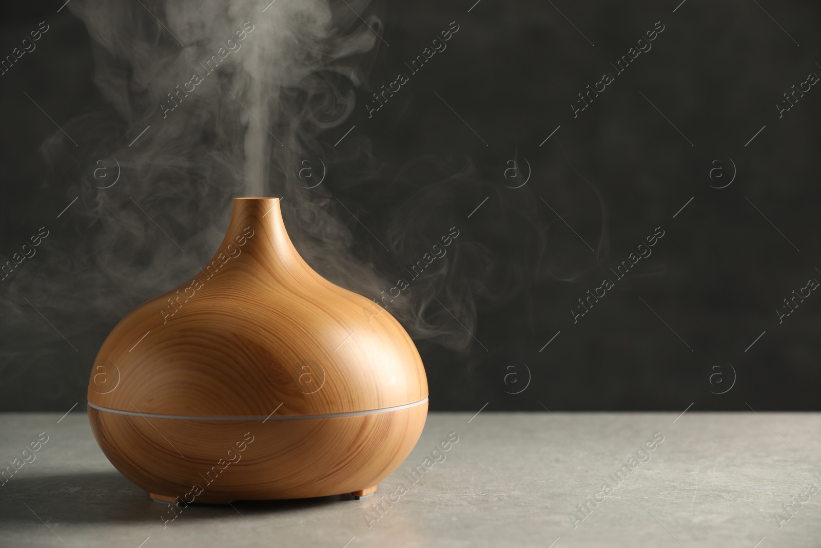 Photo of Aroma oil diffuser with steam on light grey table, space for text