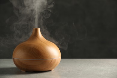 Aroma oil diffuser with steam on light grey table, space for text