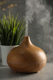 Photo of Aroma oil diffuser and plant on light grey table