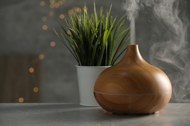 Aroma oil diffuser and plant on light grey table, space for text