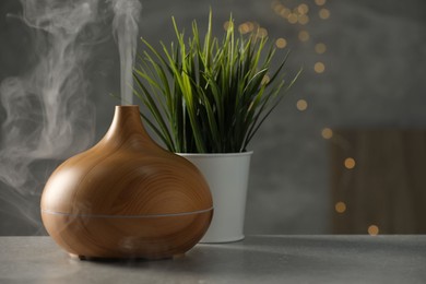 Aroma oil diffuser and plant on light grey table, space for text