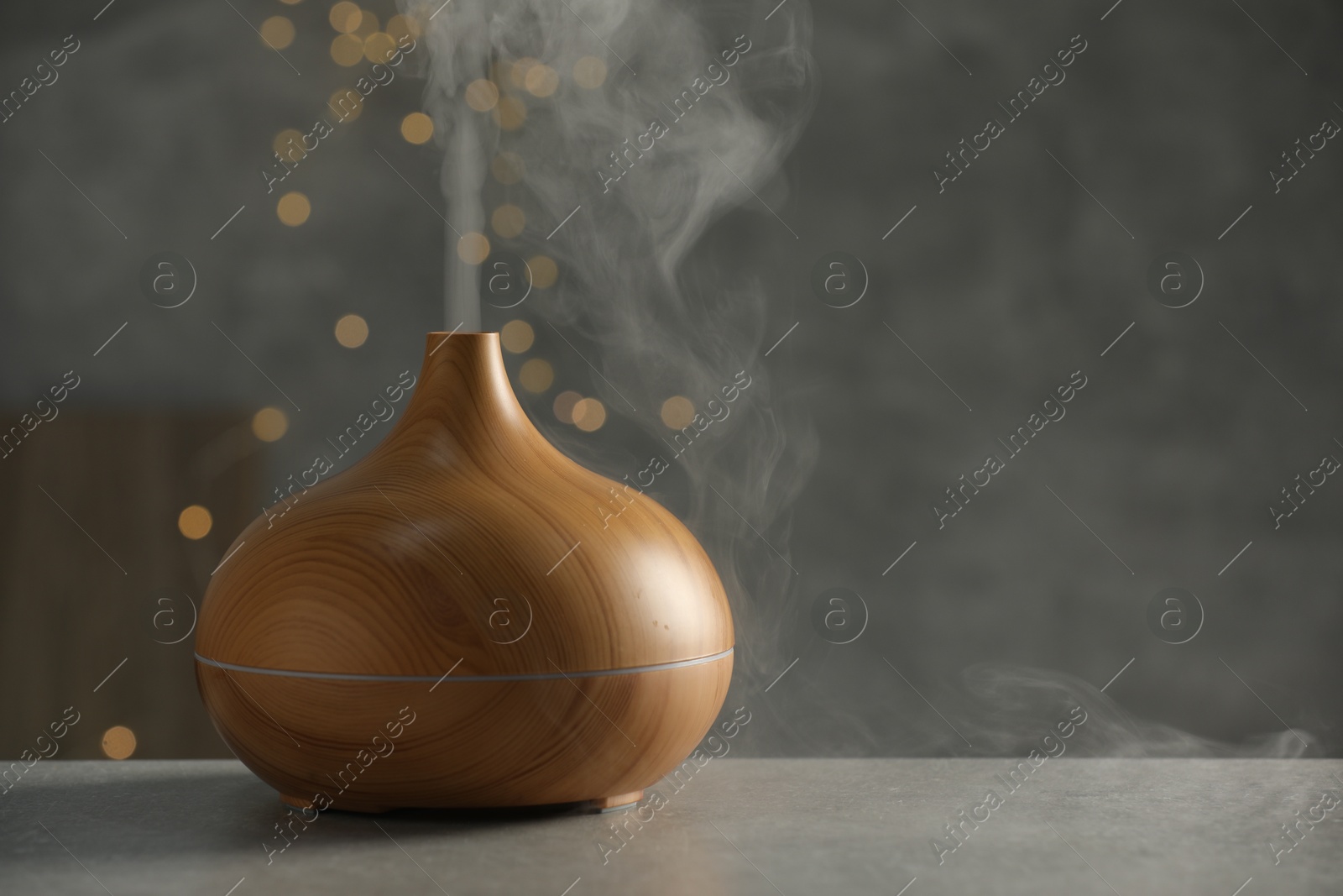 Photo of Aroma oil diffuser with steam on light grey table, space for text