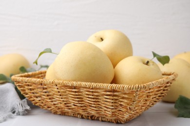 Photo of Delicious fresh apple pears in wicker basket and green leaves on white table