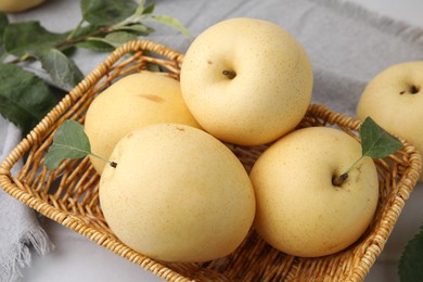 Photo of Delicious fresh apple pears in wicker basket and green leaves on table, closeup