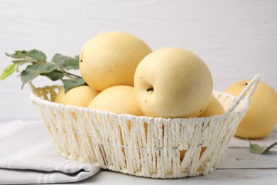 Delicious fresh apple pears in wicker basket and green leaves on white wooden table, closeup